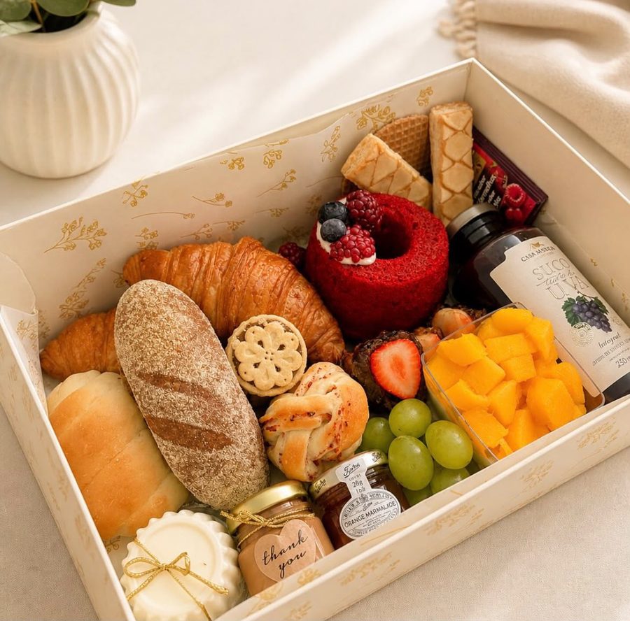 Caixa de café da manhã com pães, croissant, bolo red velvet, frutas e suco